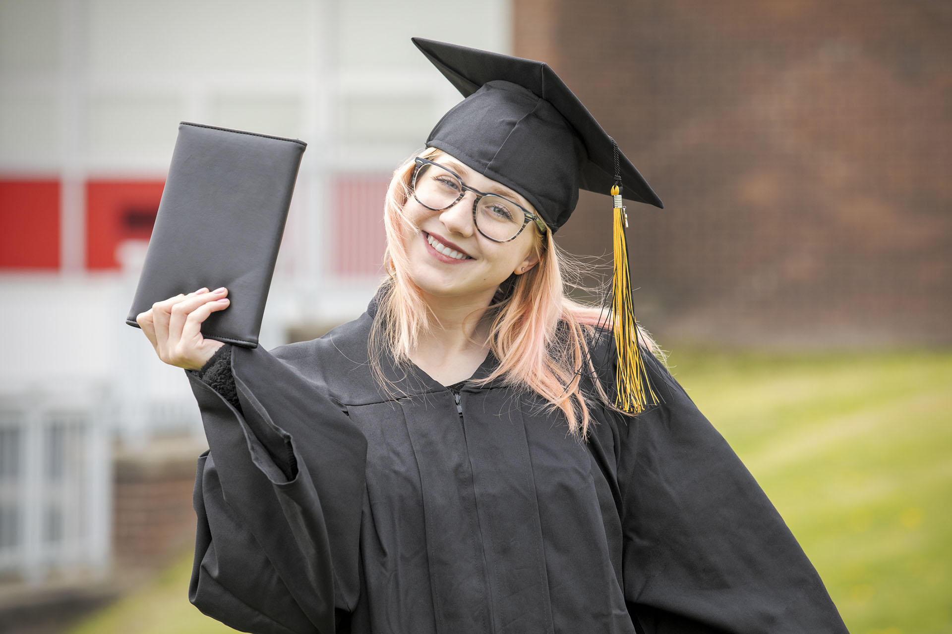 Graduate holding her diploma outdoors.